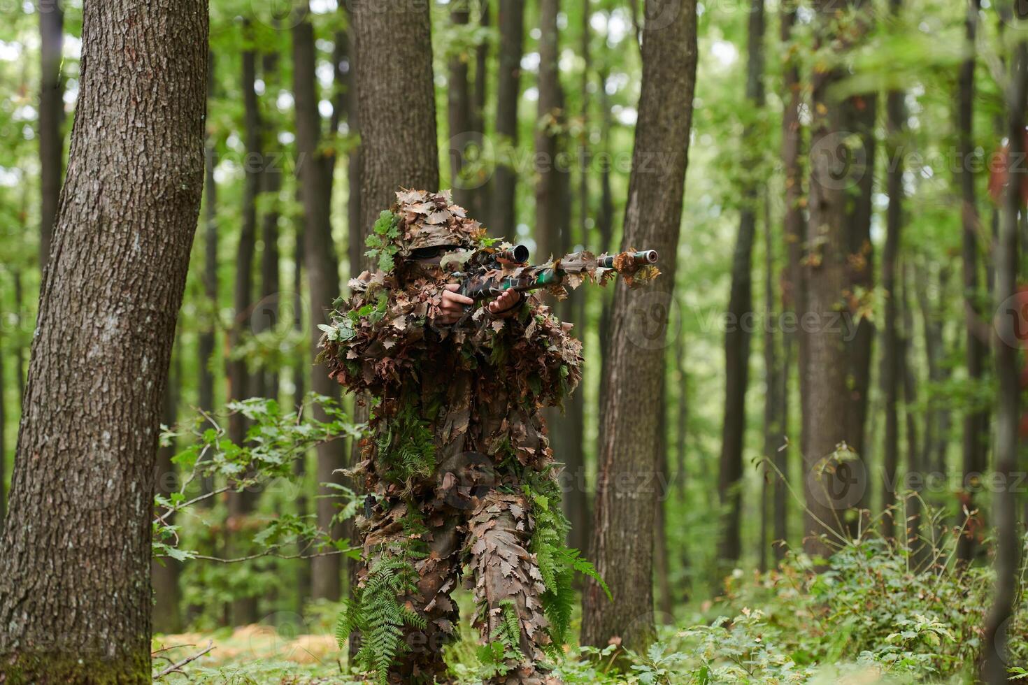 A highly skilled elite sniper, camouflaged in the dense forest, stealthily maneuvers through dangerous woodland terrain on a covert and precise mission photo