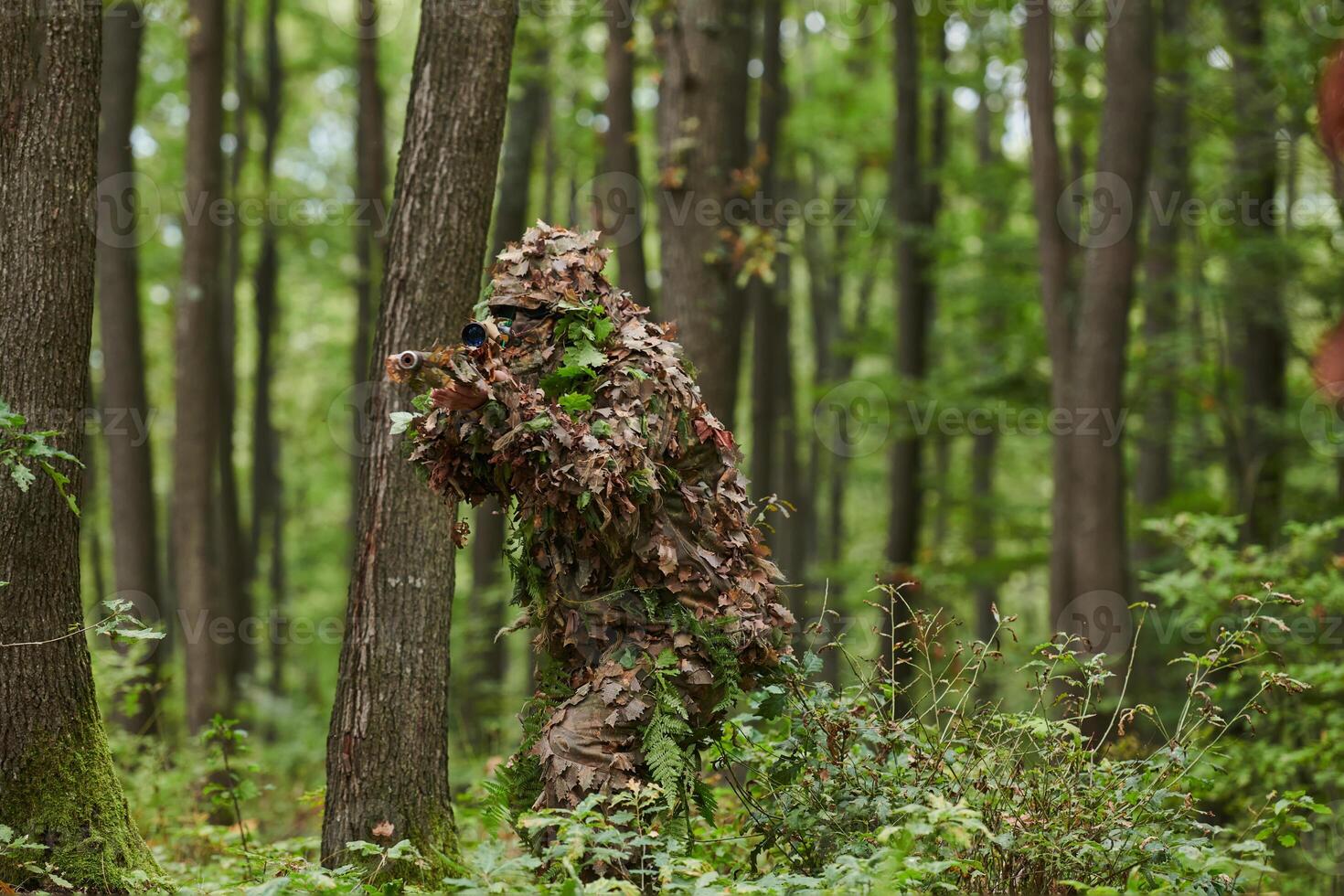 A highly skilled elite sniper, camouflaged in the dense forest, stealthily maneuvers through dangerous woodland terrain on a covert and precise mission photo