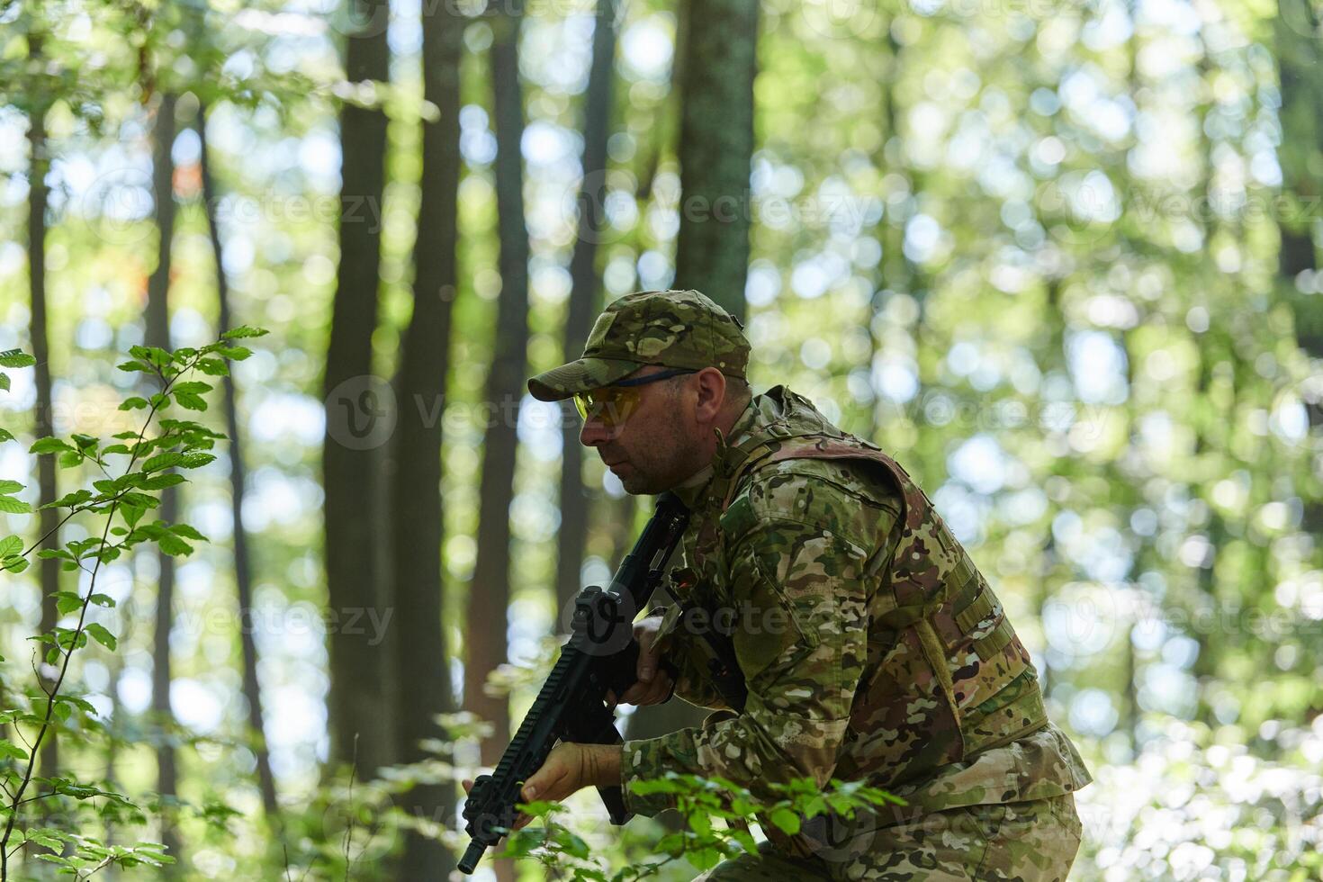 An elite soldier, camouflaged and stealthily navigating through dangerous woodland terrain, executes a covert mission in a secluded forest area photo