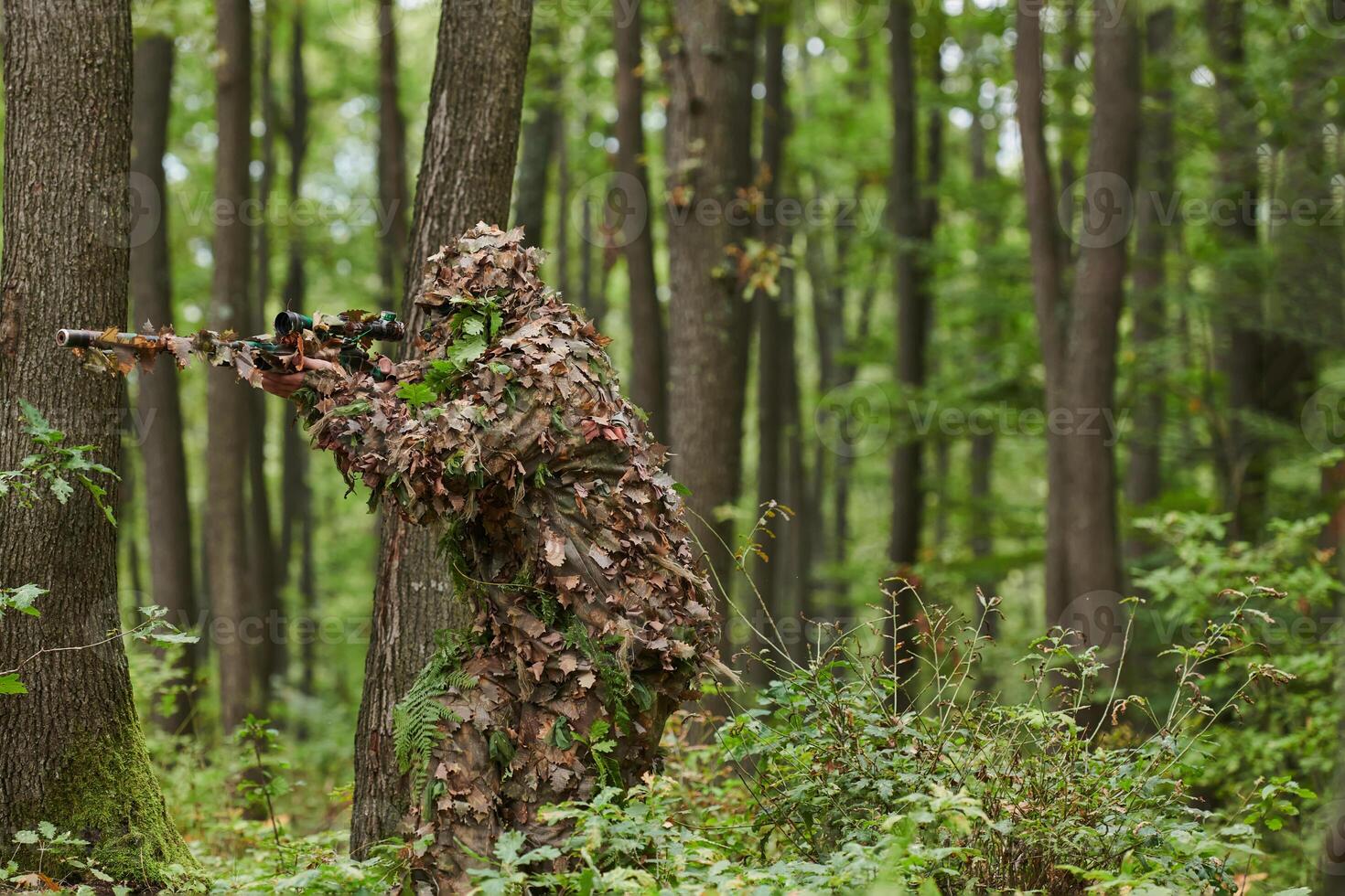 A highly skilled elite sniper, camouflaged in the dense forest, stealthily maneuvers through dangerous woodland terrain on a covert and precise mission photo