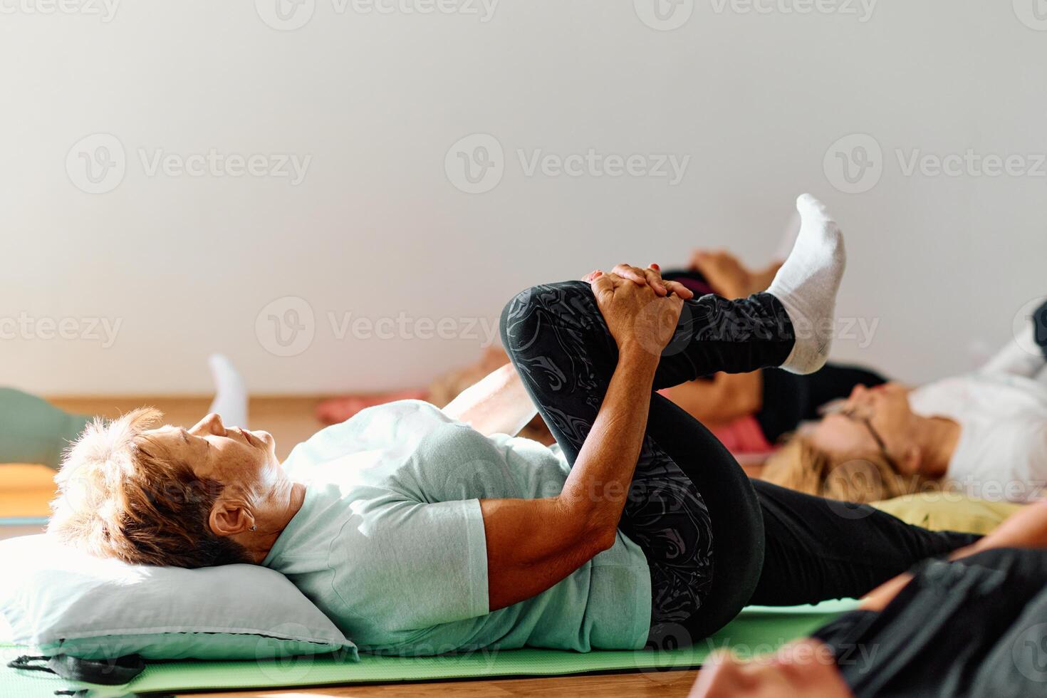 In a sunlit space, a senior woman gracefully practices rejuvenating yoga, focusing on neck, back, and leg stretches, embodying serenity and well-being photo