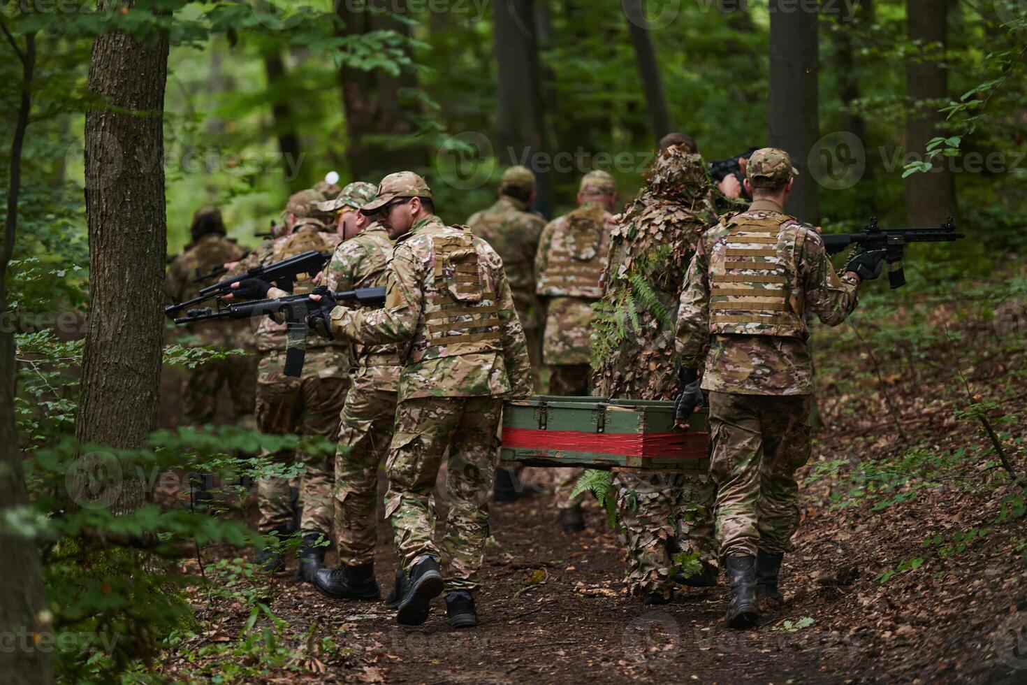 Elite military unit, cloaked in camouflage, transports a crate of ammunition through the dense forest, epitomizing strategic readiness and precision in their covert mission photo