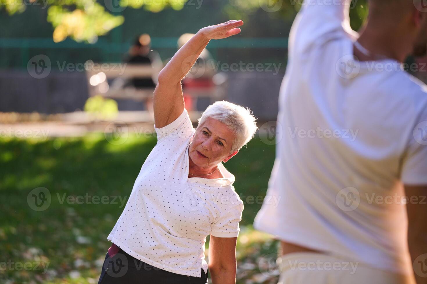 A group of seniors follows a trainer, engaging in outdoor exercises in the park, as they collectively strive to maintain vitality and well-being, embracing an active and health-conscious lifestyle in photo