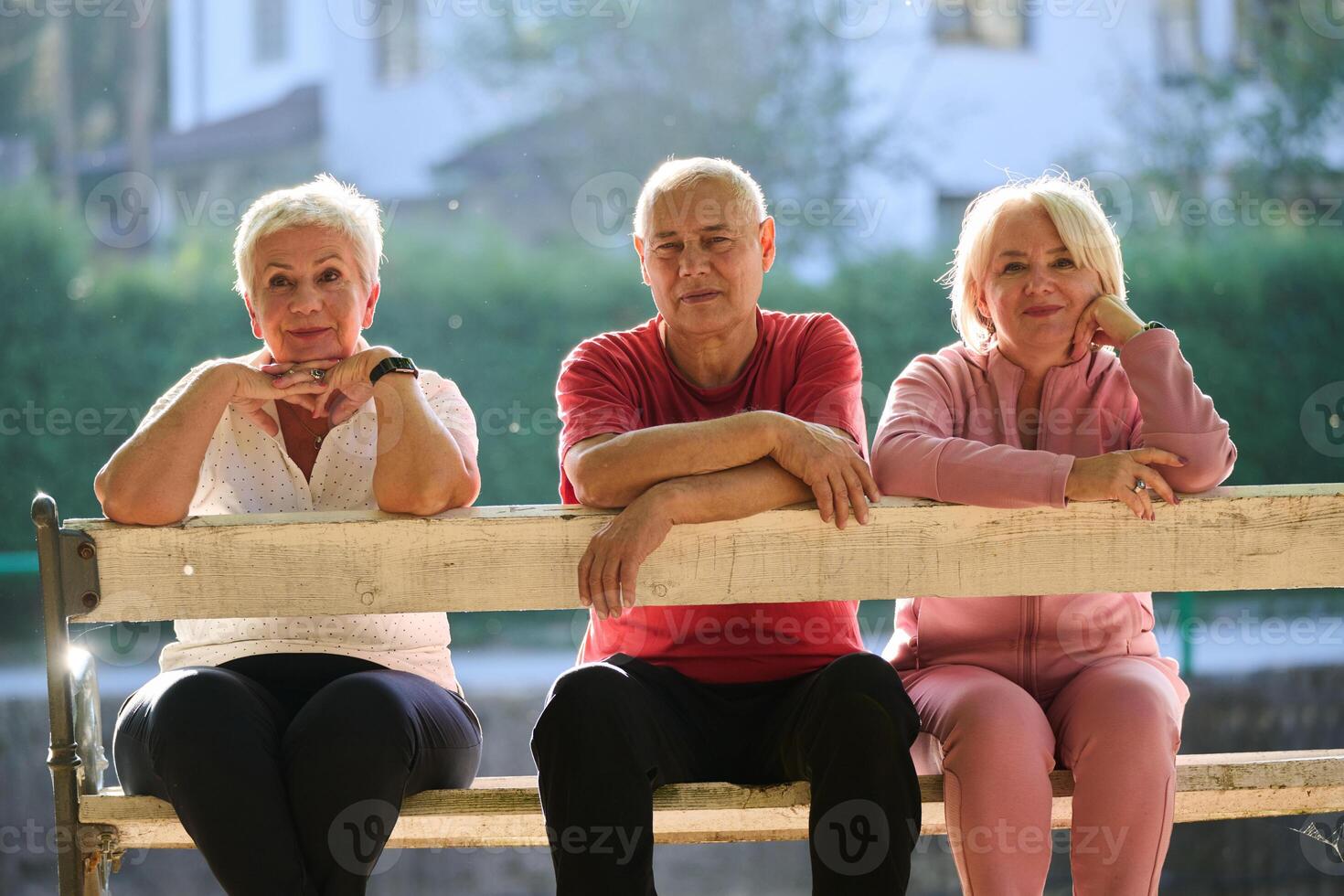 A group of elderly individuals, including a senior man and two older women, sits in a park on a sunny autumn day, embodying the concept of healthy aging through companionship, relaxation, and outdoor photo