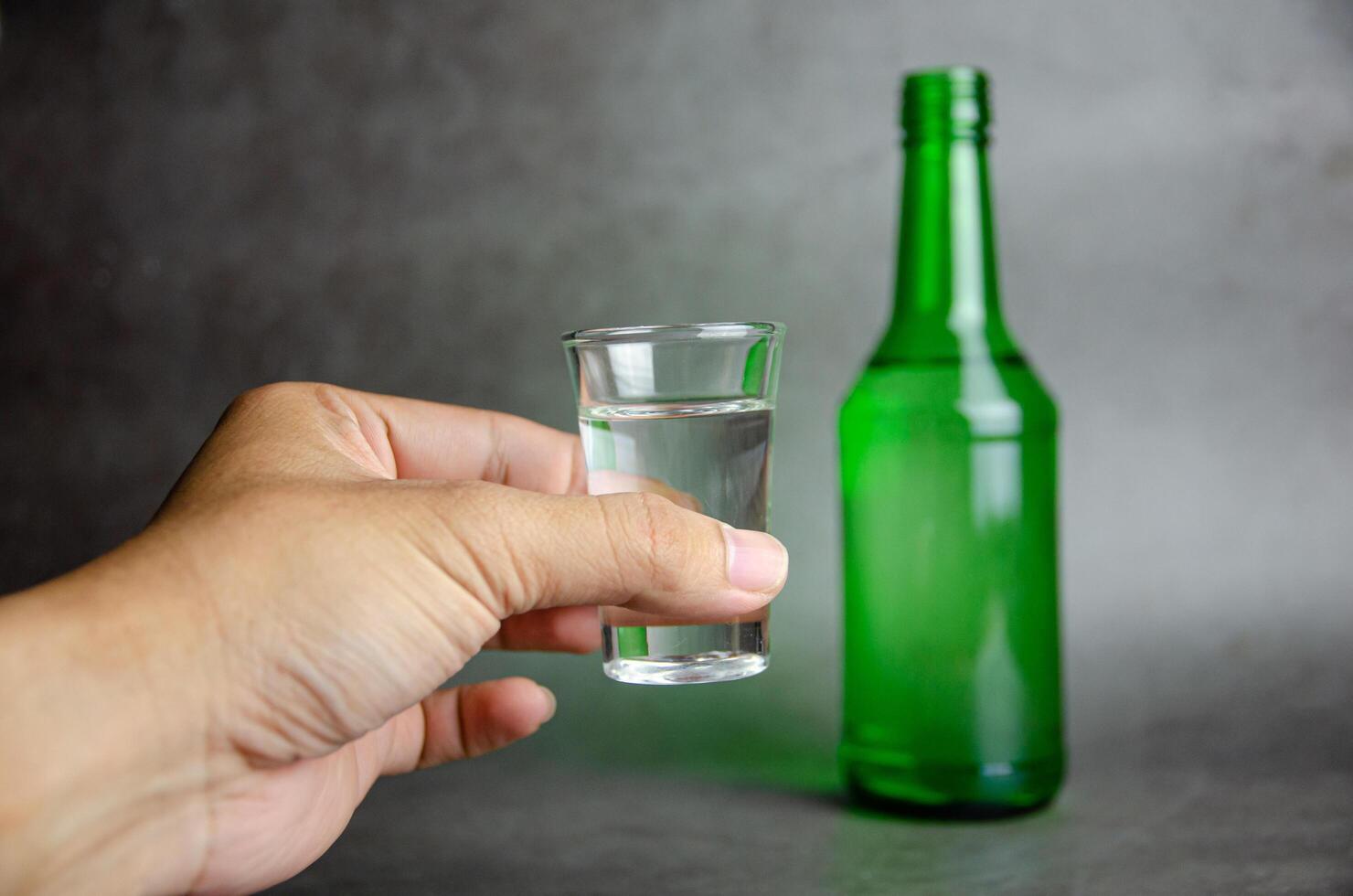 soju bottle on grey background with hand, selective focus photo