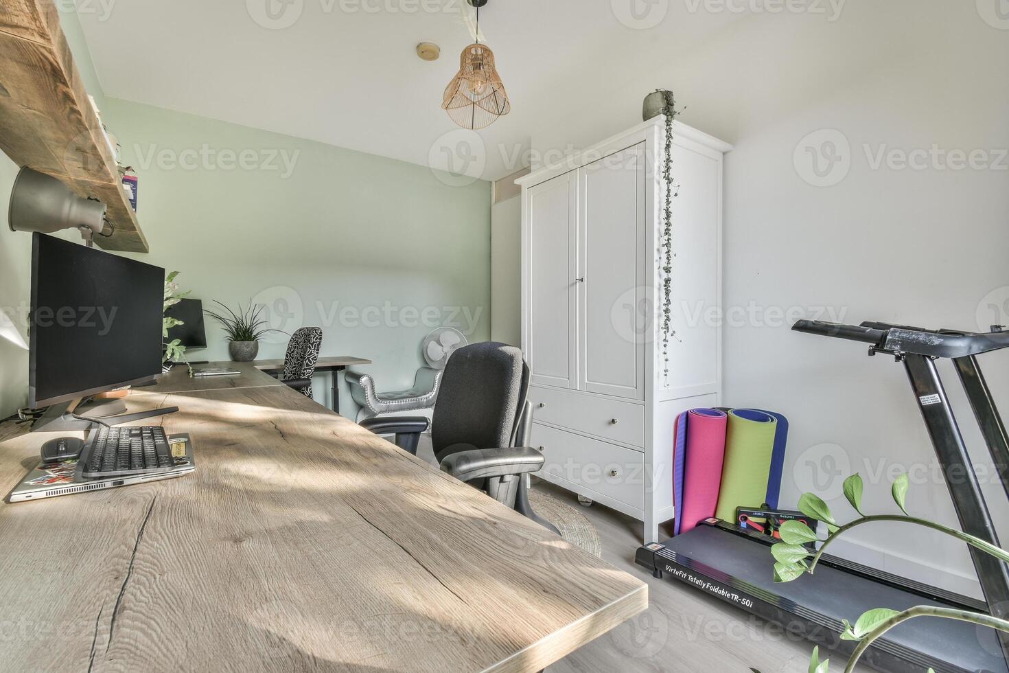 A home office with a desk, computer, and treadmill photo