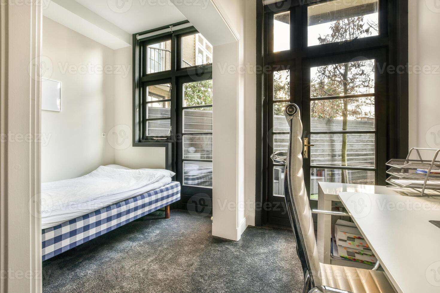 A bedroom with a bed and desk in front of a window photo