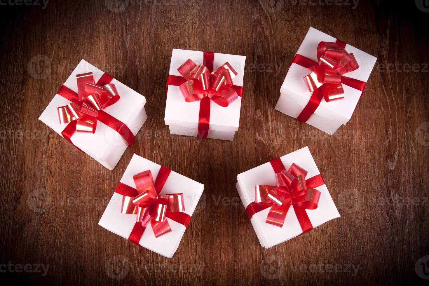 five white festive gift boxes with red bows on a wooden table photo