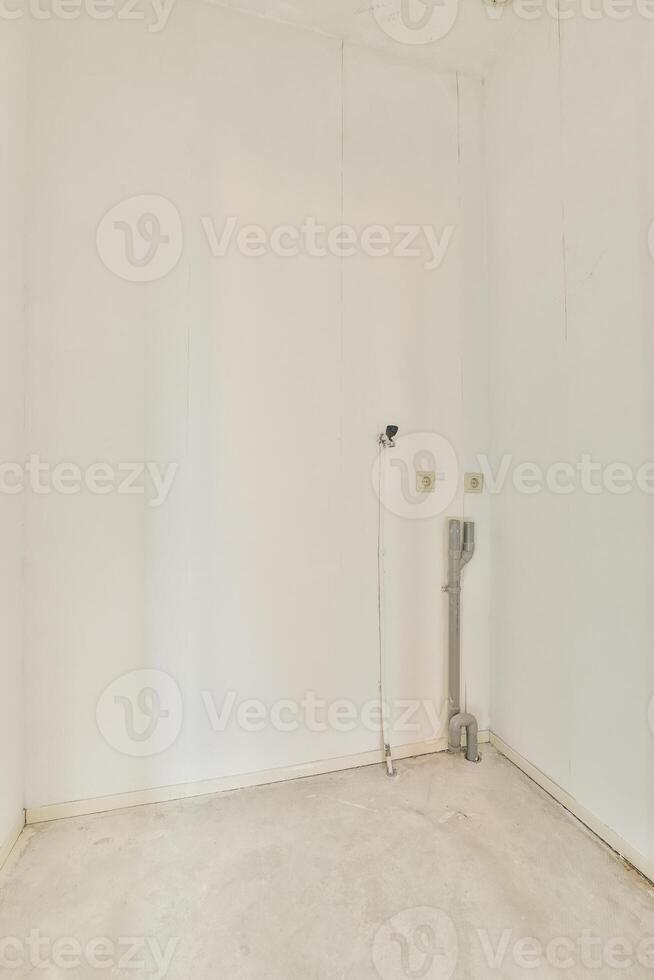 An empty room with a white wall and a toilet photo
