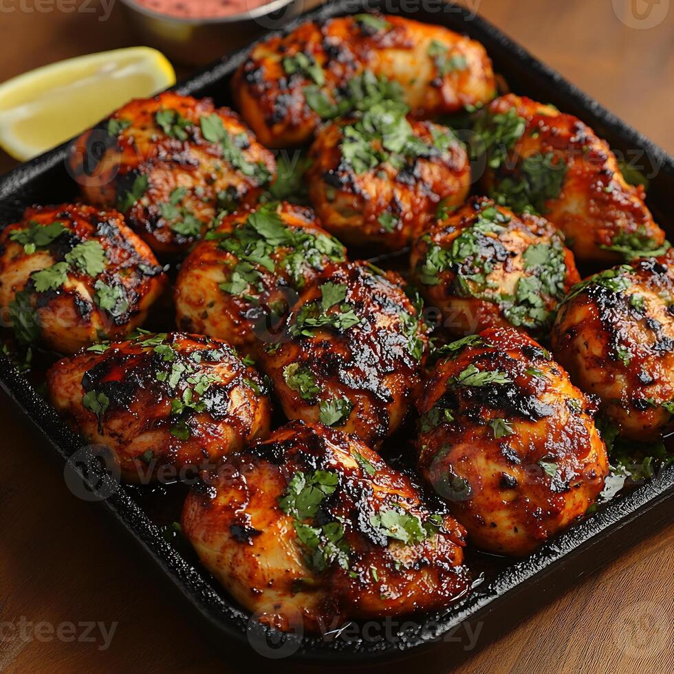 Hot tandoori chicken sizzling a platter garnished with lemon wedges and mint chutney ready to be served photo