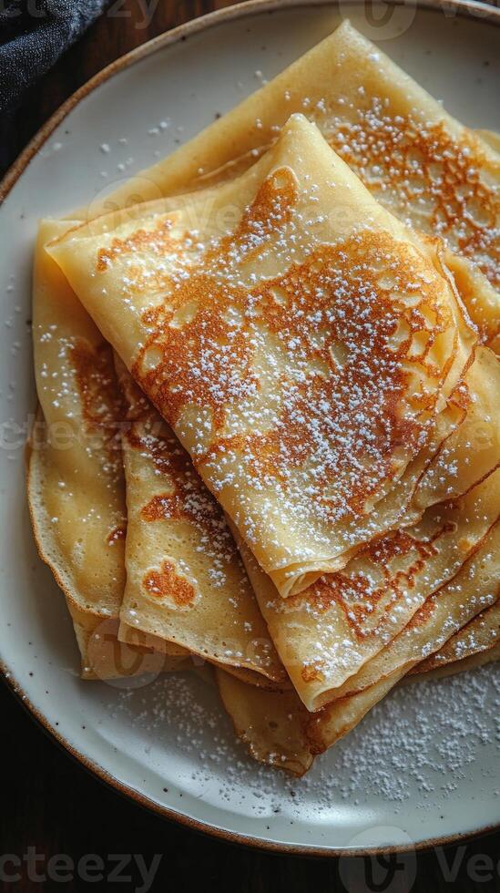 Thin crepes dusted with powdered sugar layered on plate photo