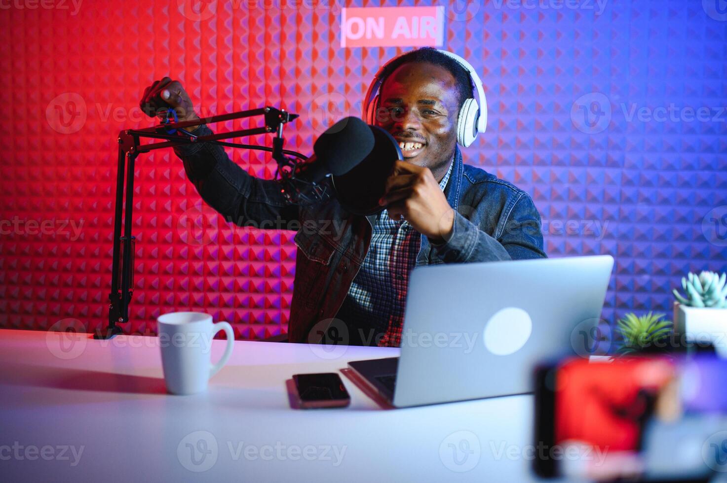 african american vlogger using smartphone to film podcast in studio. blogger with mobile phone, microphone and headphones filming photo