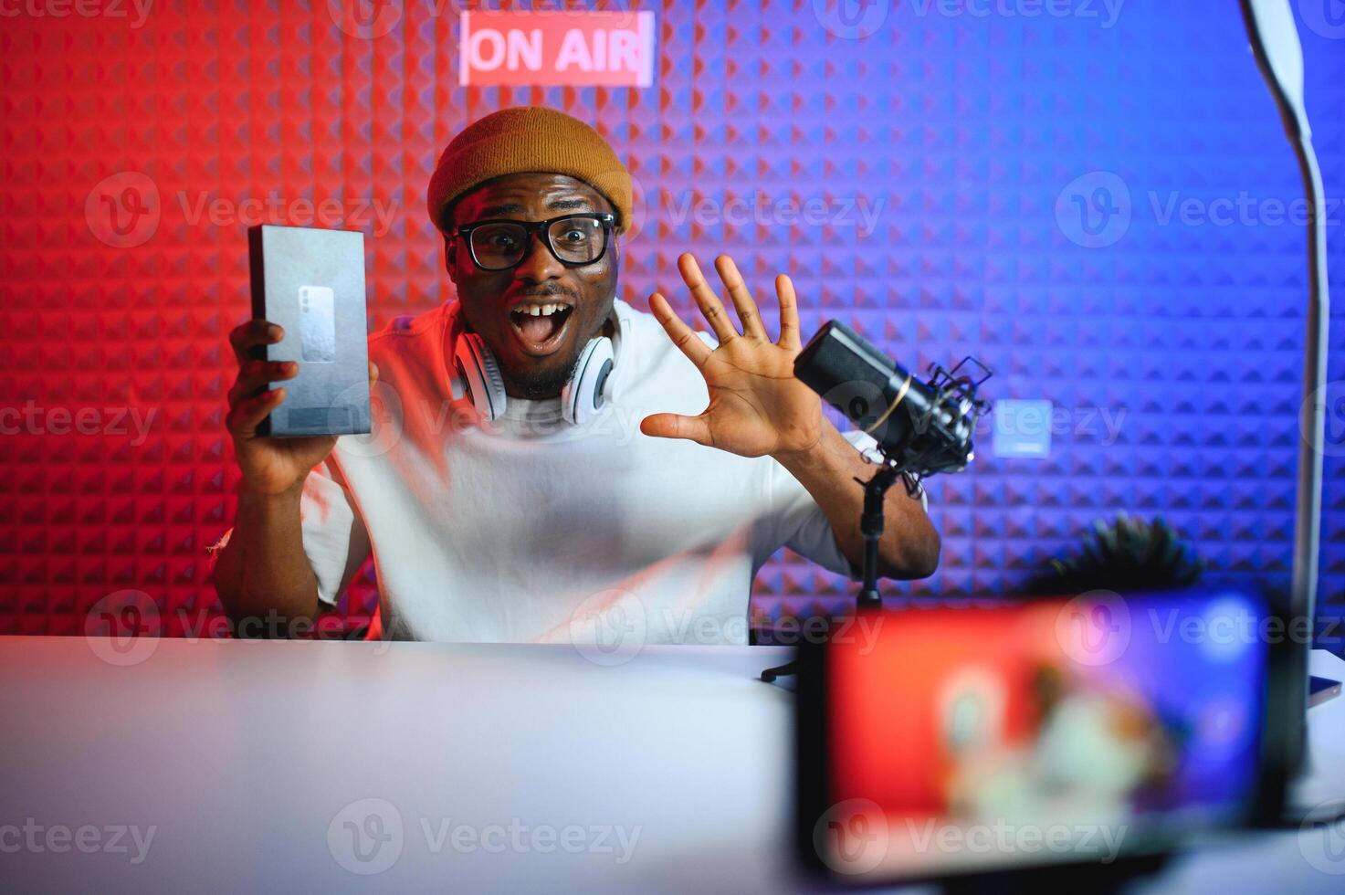 african american vlogger using smartphone to film podcast in studio. blogger with mobile phone, microphone and headphones filming photo