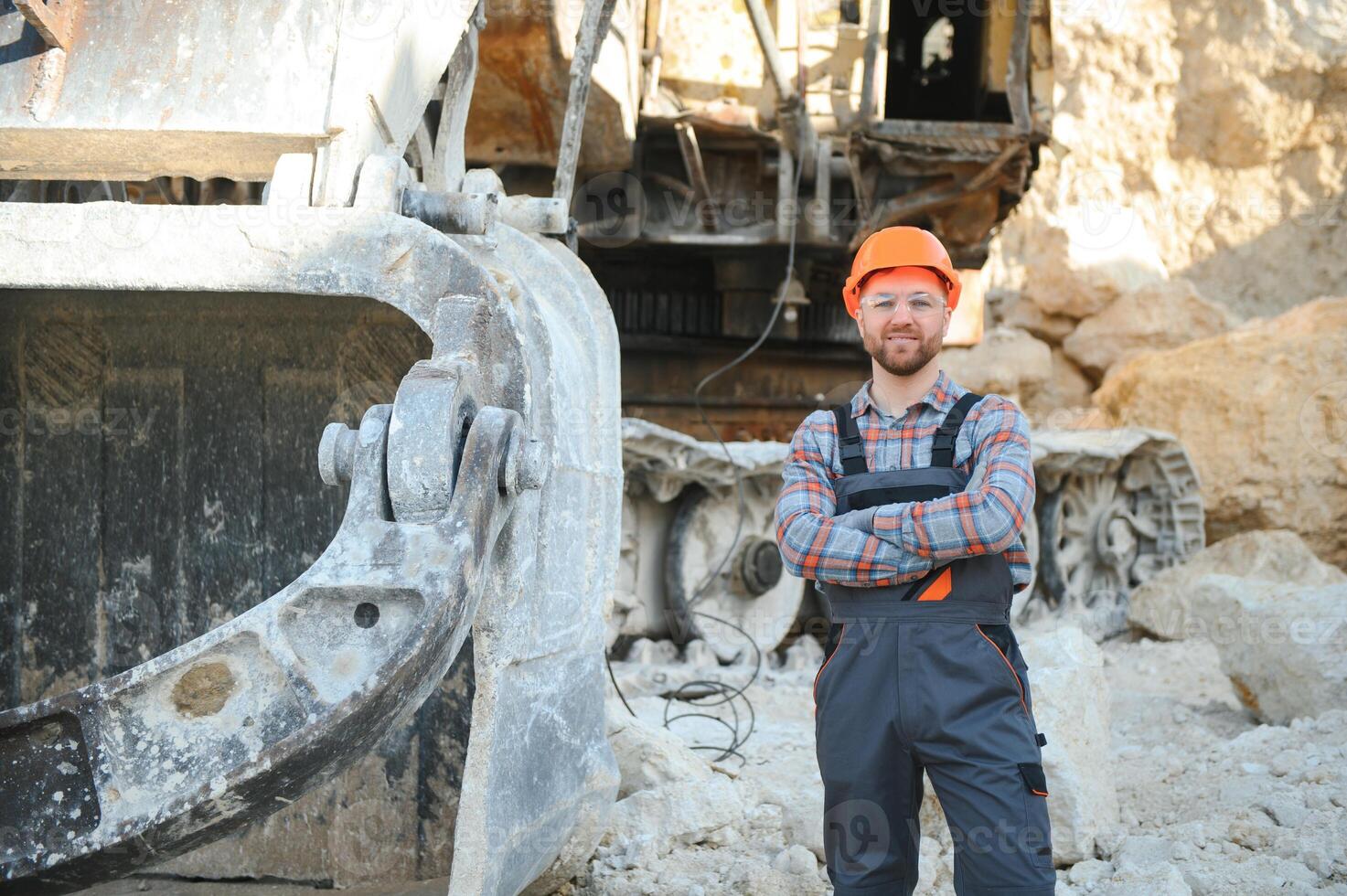 A worker in a helmet stands on the background of an excavator in a quarry photo