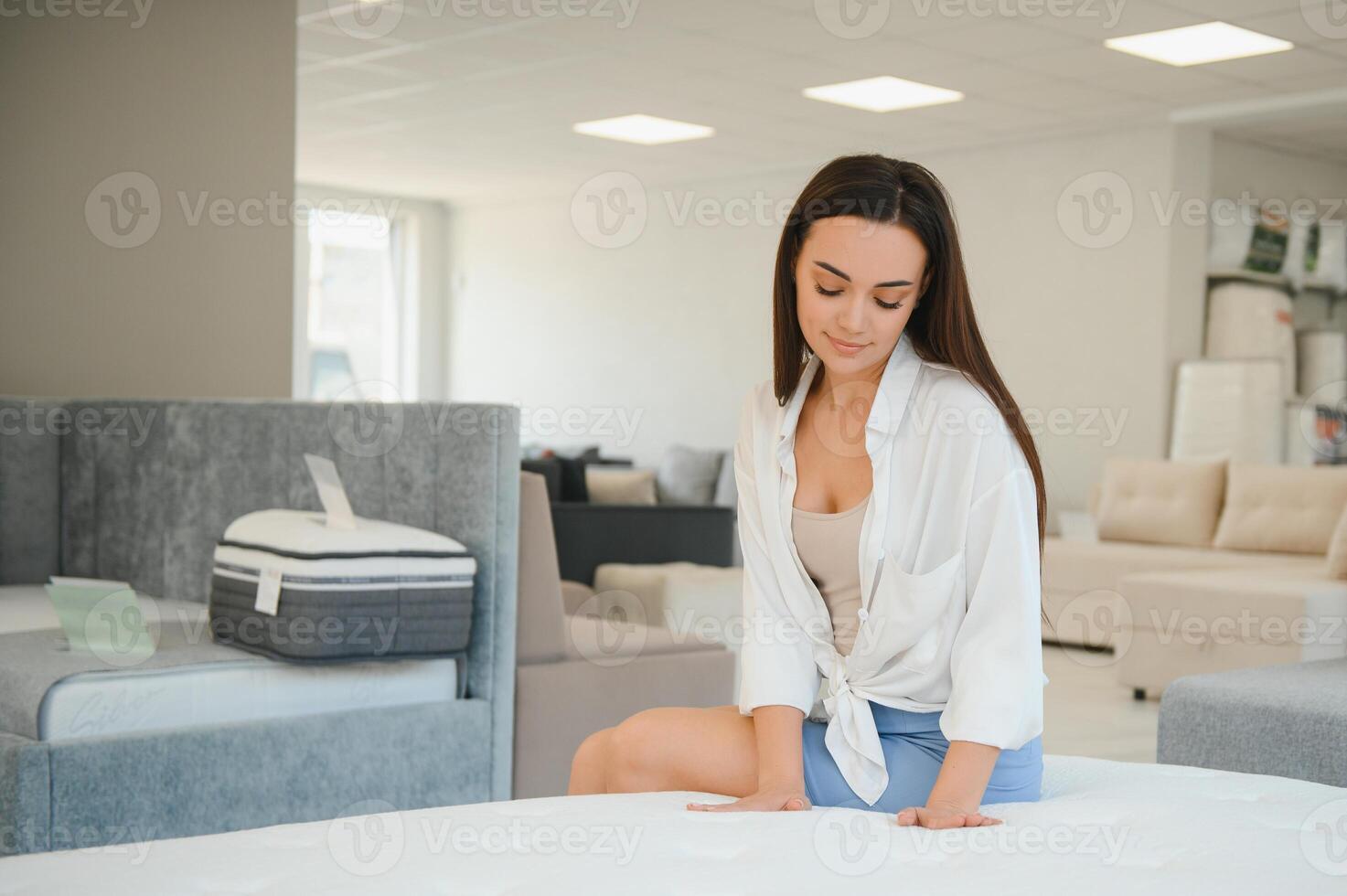 A woman in a white shirt in a mattress store. She examines the mattress she wants to buy photo