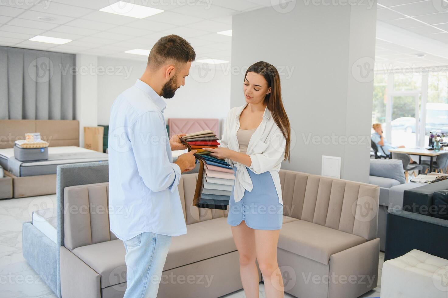 Couple choose soft corner in furniture store. Husband examines set of upholstery fabric samples photo
