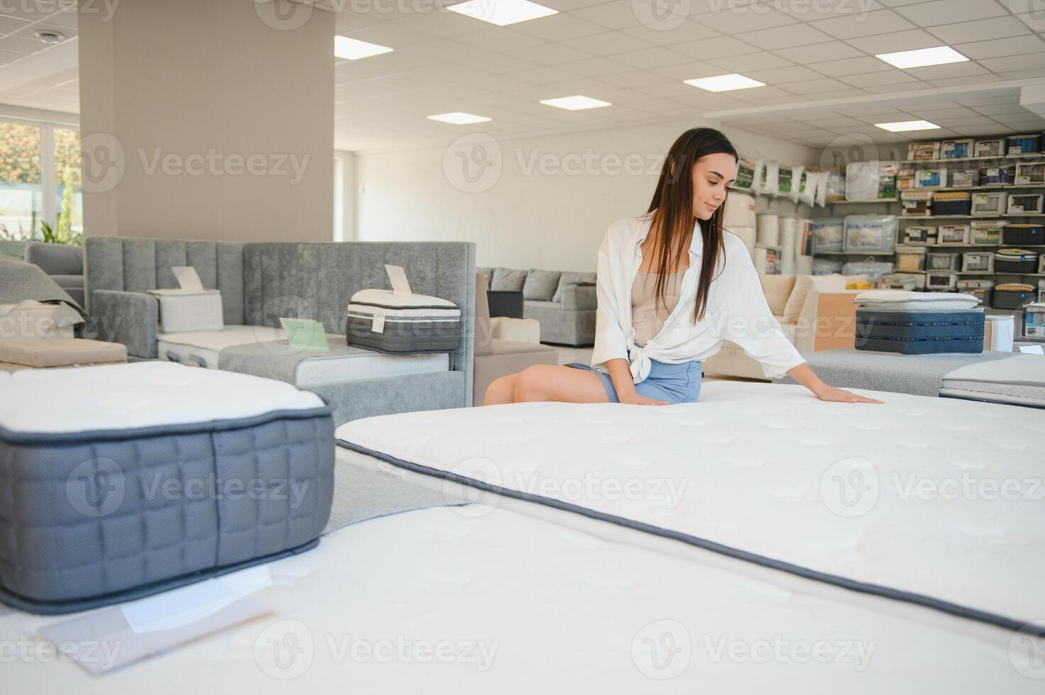 happy brunette female is sitting on mattress for testing it in the store photo
