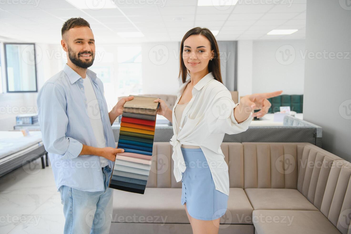 Couple of young man and woman shoppers choose sofa in living room department of furniture store photo
