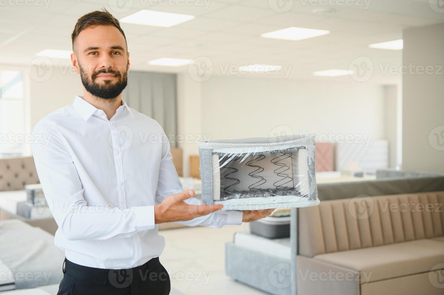 A young seller in a furniture store showing samples of mattresses in a bed photo