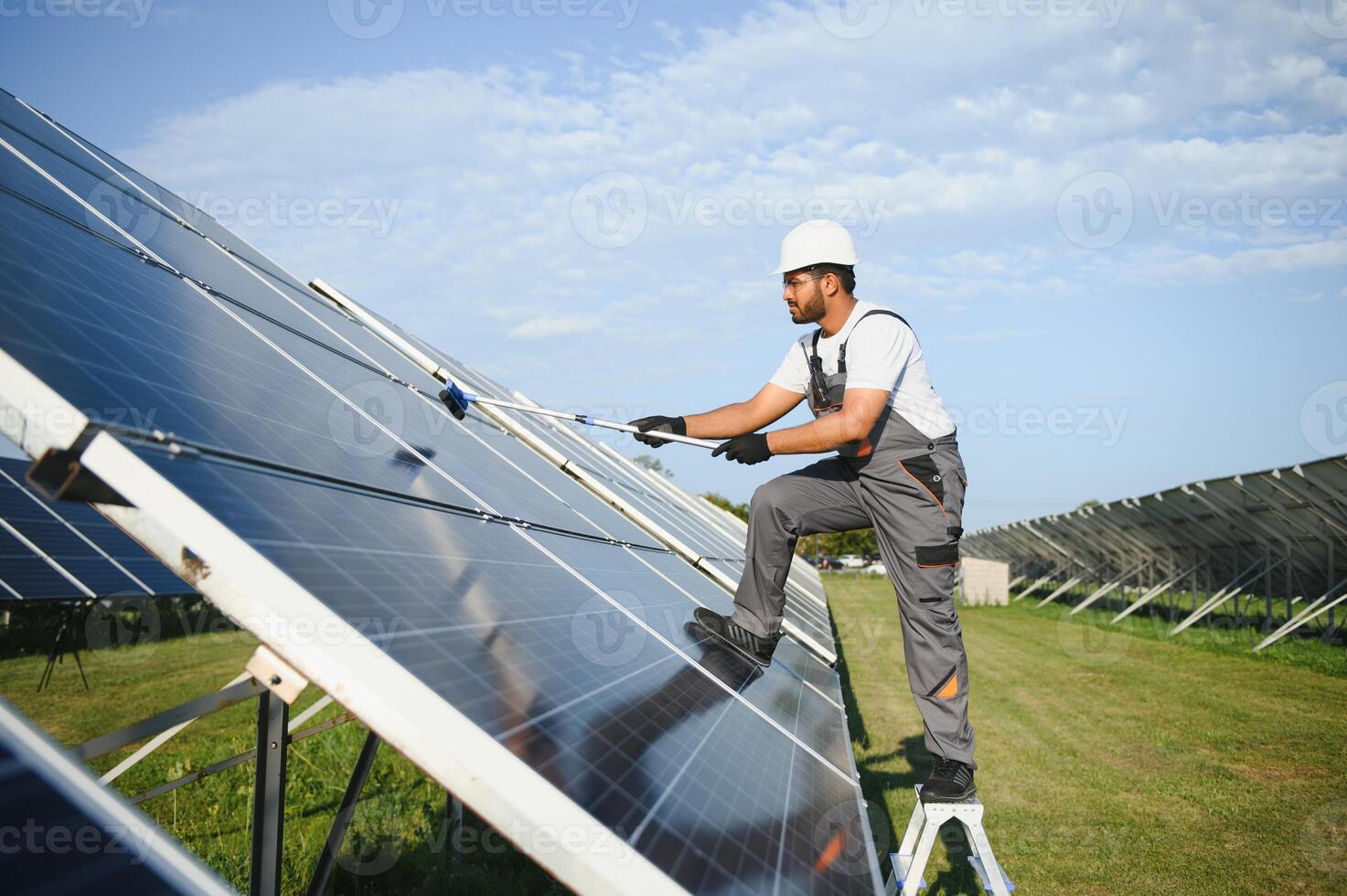 Professional indian worker cleans solar panels with brush, green electric power technology photo