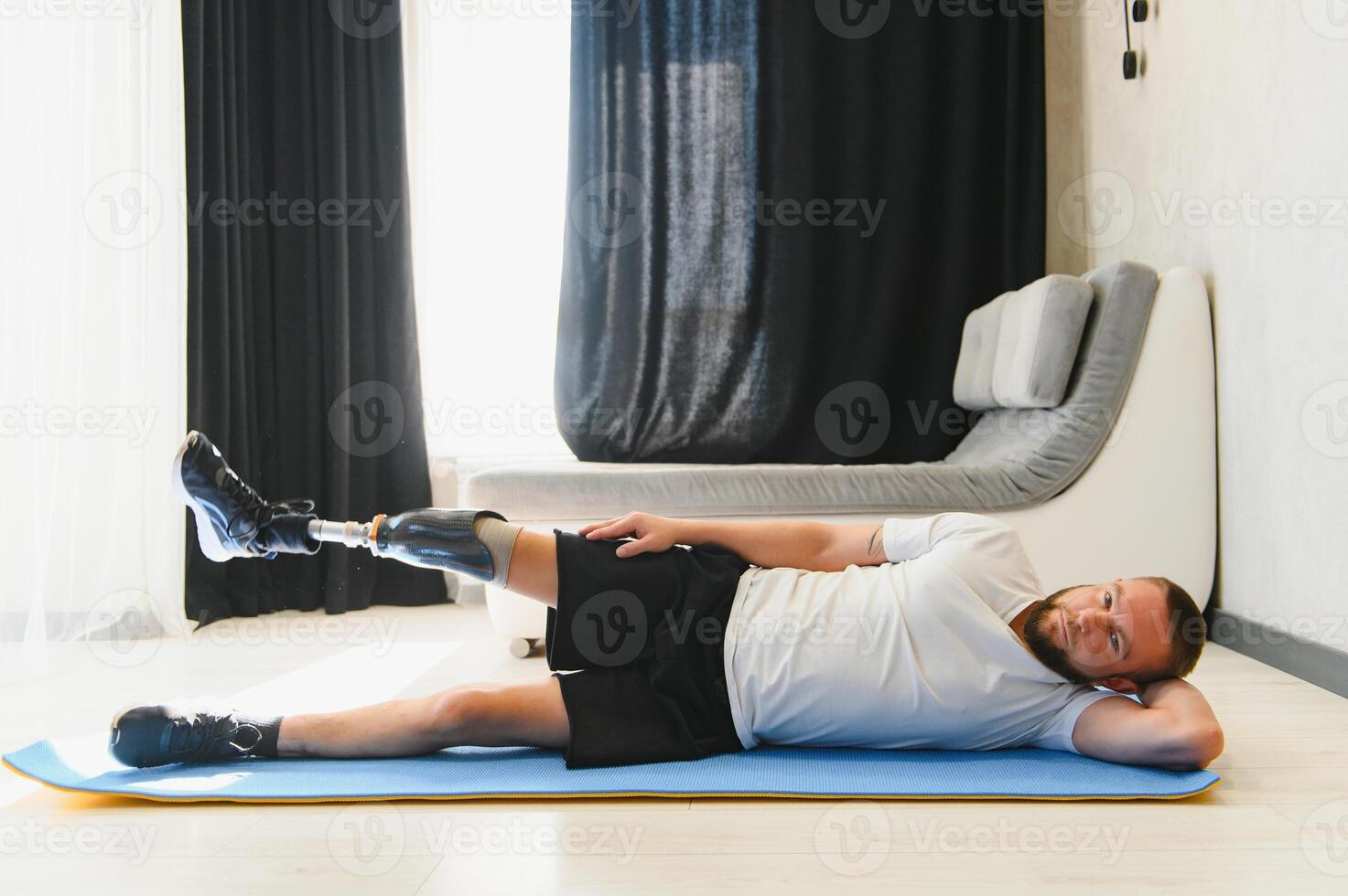 Full length portrait of man with prosthetic leg doing stretching exercises at home and reaching toes photo