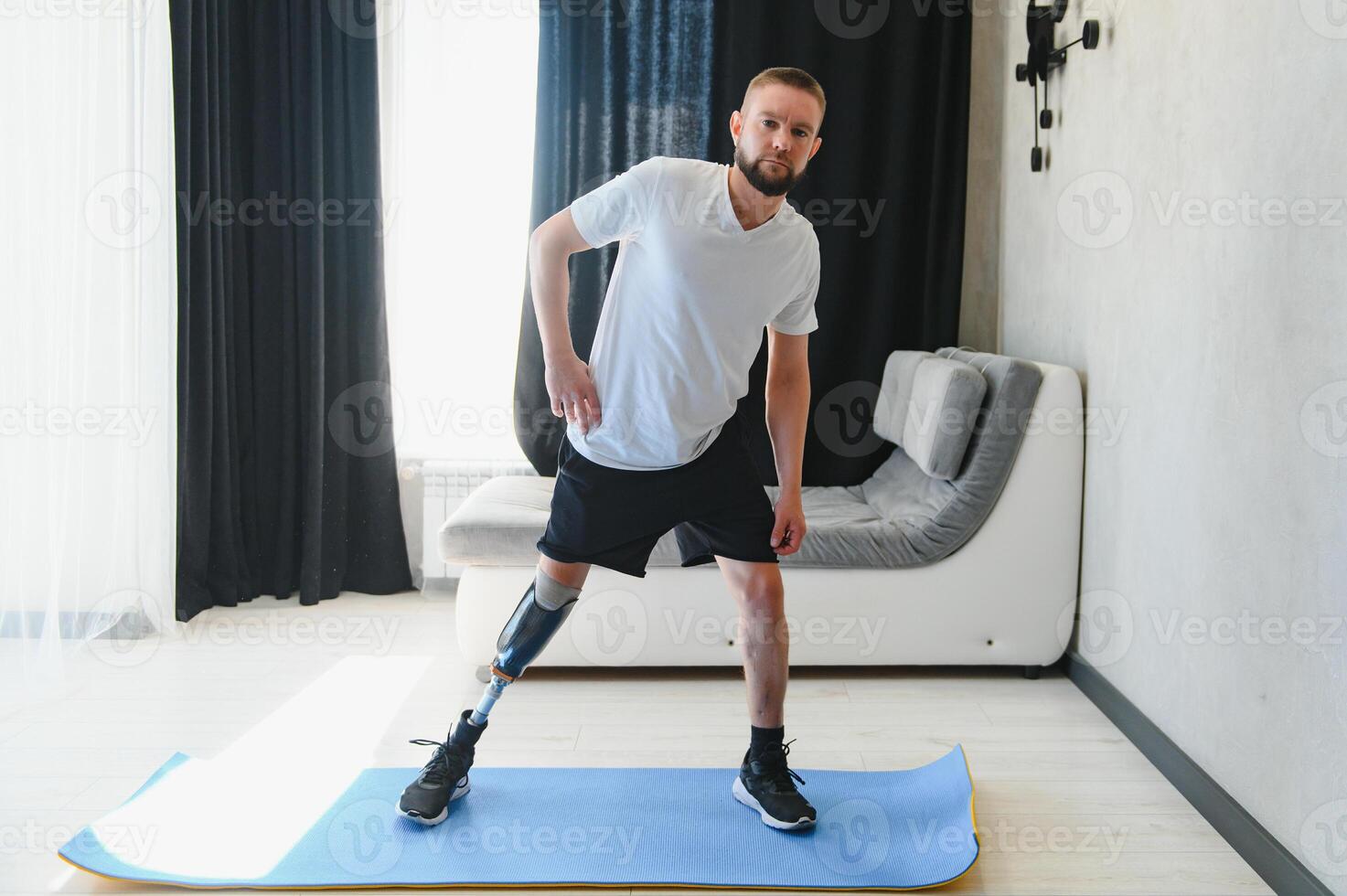Man amputee with prosthetic leg disability on transfemoral leg prosthesis artificial device making stretching rehabilitation physical exercise at home. People w amputation disabilities everyday life photo
