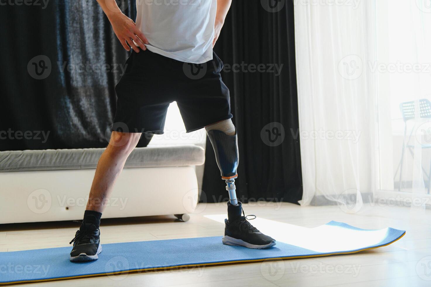 Full length portrait of man with prosthetic leg doing stretching exercises at home and reaching toes photo