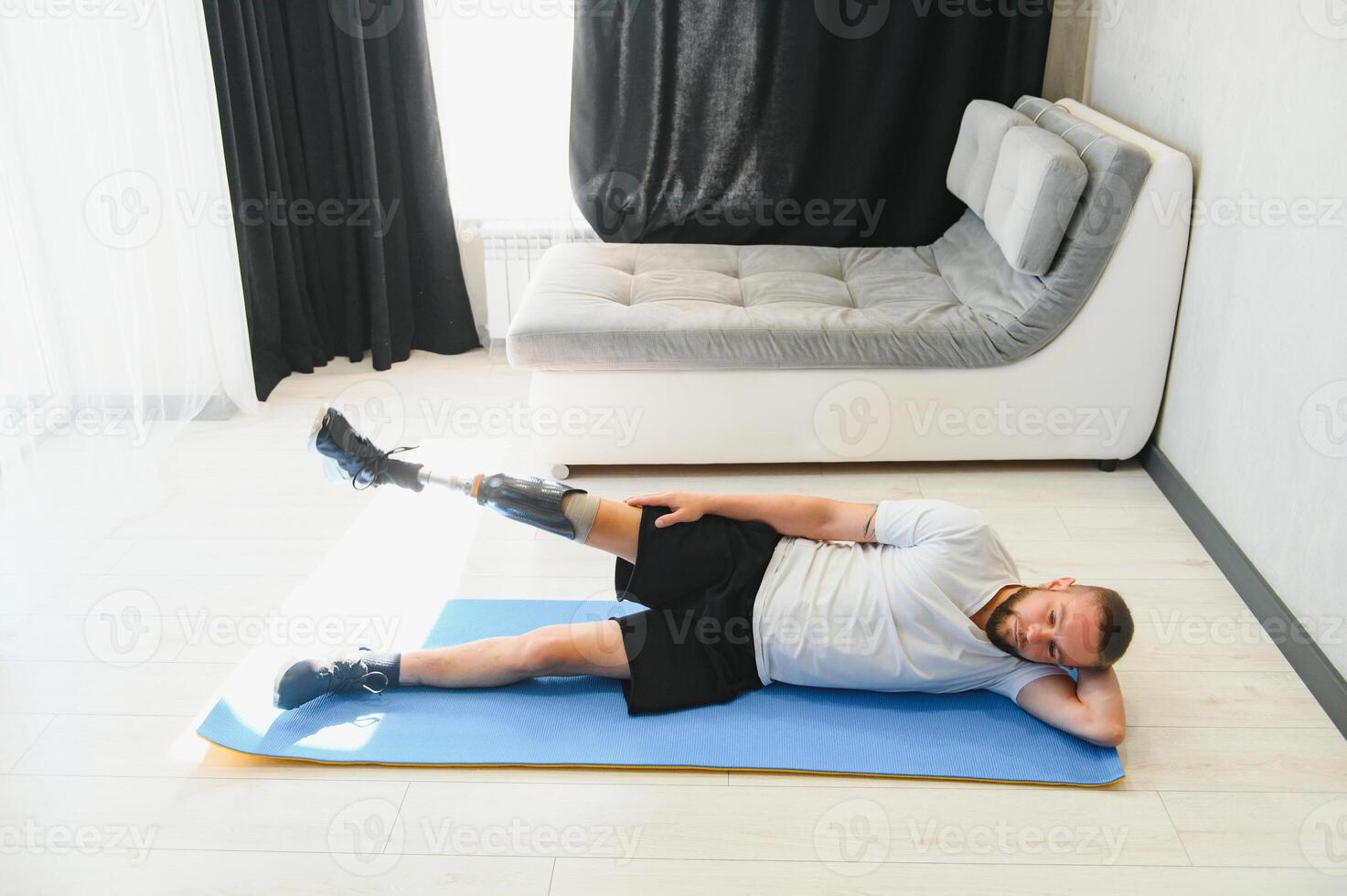 Full length portrait of man with prosthetic leg doing stretching exercises at home and reaching toes photo