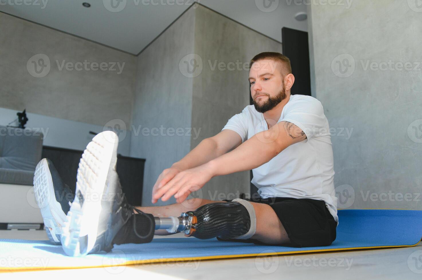 Full length portrait of man with prosthetic leg doing stretching exercises at home and reaching toes photo