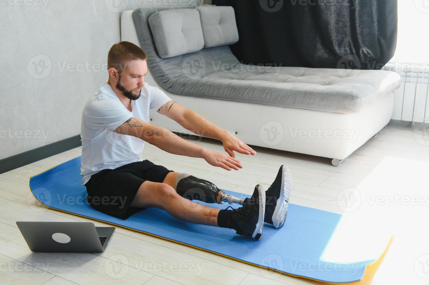 man exercising online stretching his legs at home, with amputated leg prosthesis photo