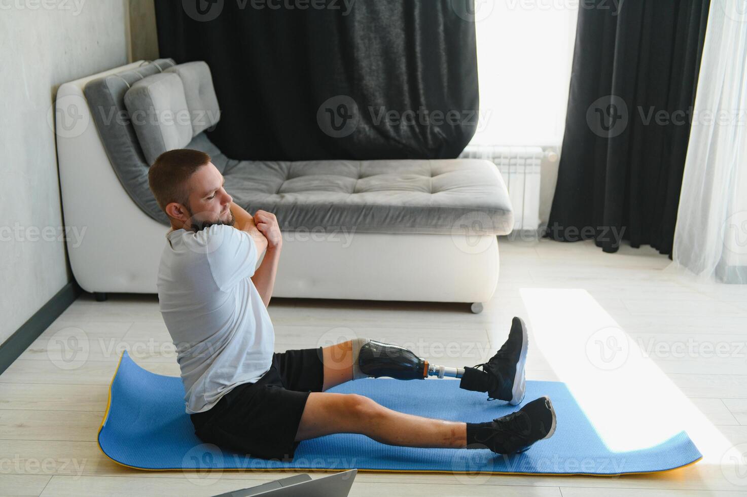 man exercising online stretching his legs at home, with amputated leg prosthesis photo