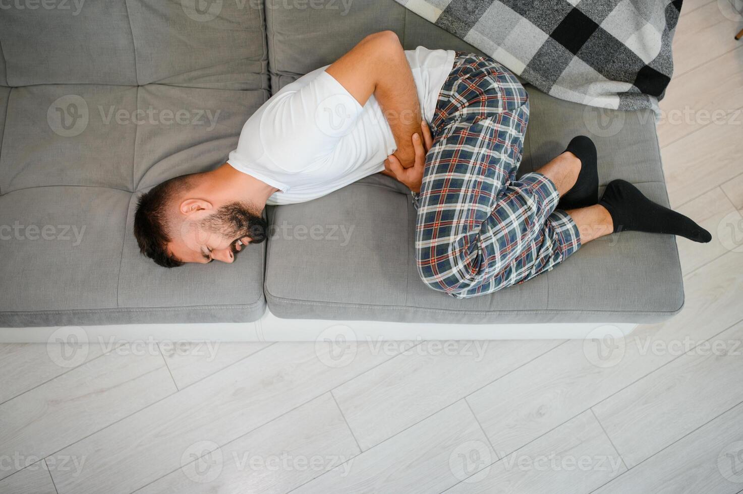 Handsome young man suffering from stomach ache while lying on sofa at home photo