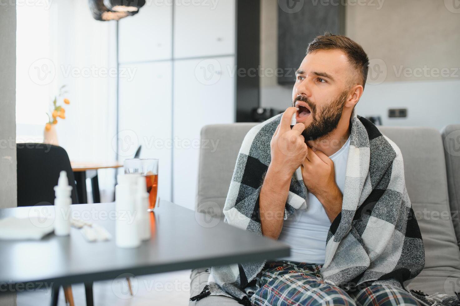 rhinitis, medicine and healthcare concept, sick man in blanket using oral spray at home. photo