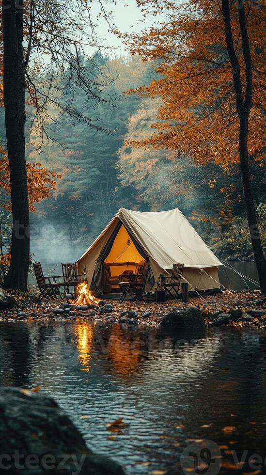 Illuminated tent camping by misty river in autumn forest photo