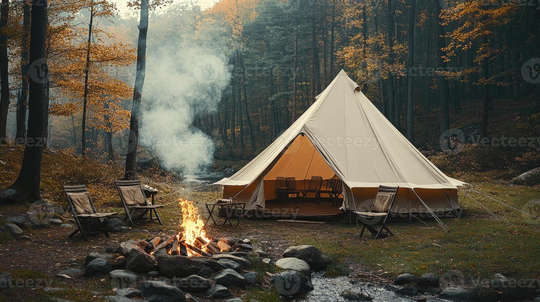 Large canvas bell tent camping beside forest river at dusk with campfire burning photo