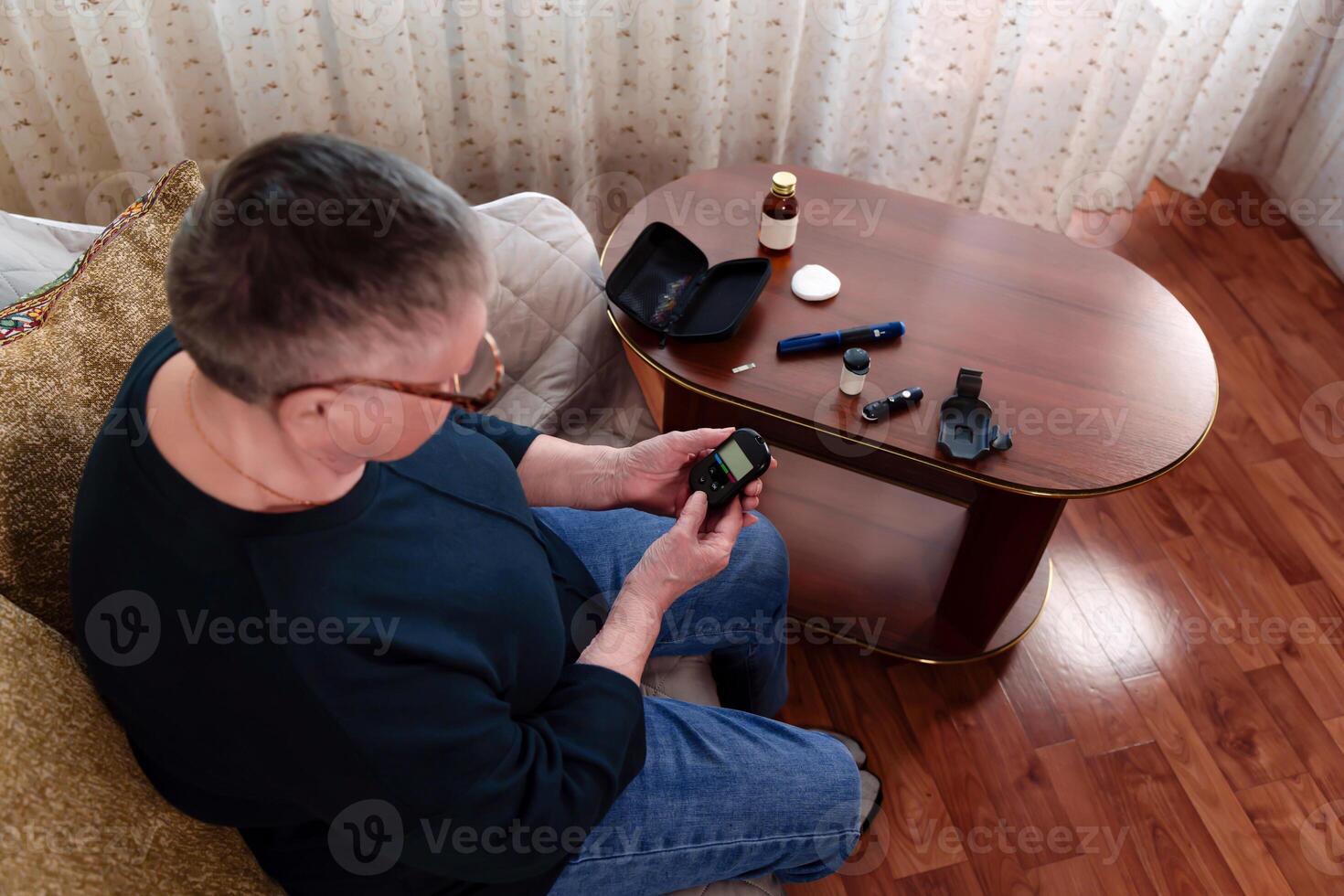 Focused and determined, an elderly grandmother in glasses and short gray hair examines the readings of a glucometer, demonstrating her commitment to maintaining control over her blood sugar levels photo