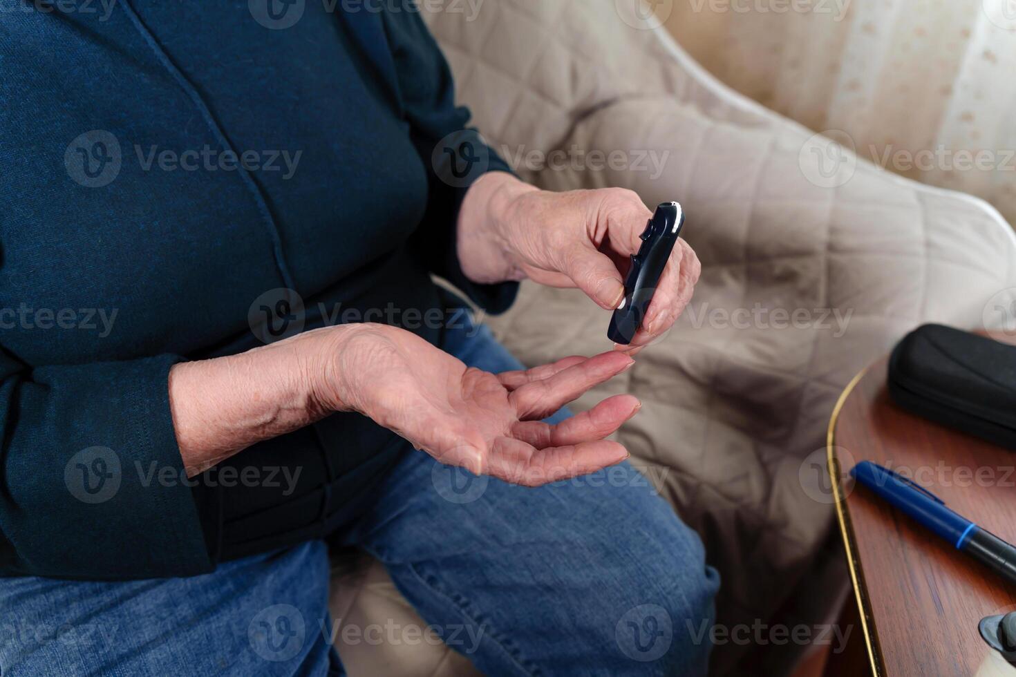 Closeup of an elderly woman's wrinkled hands holding a lancet, monitoring her blood sugar levels through a self-testing device. Concept of diabetes management and senior health care photo
