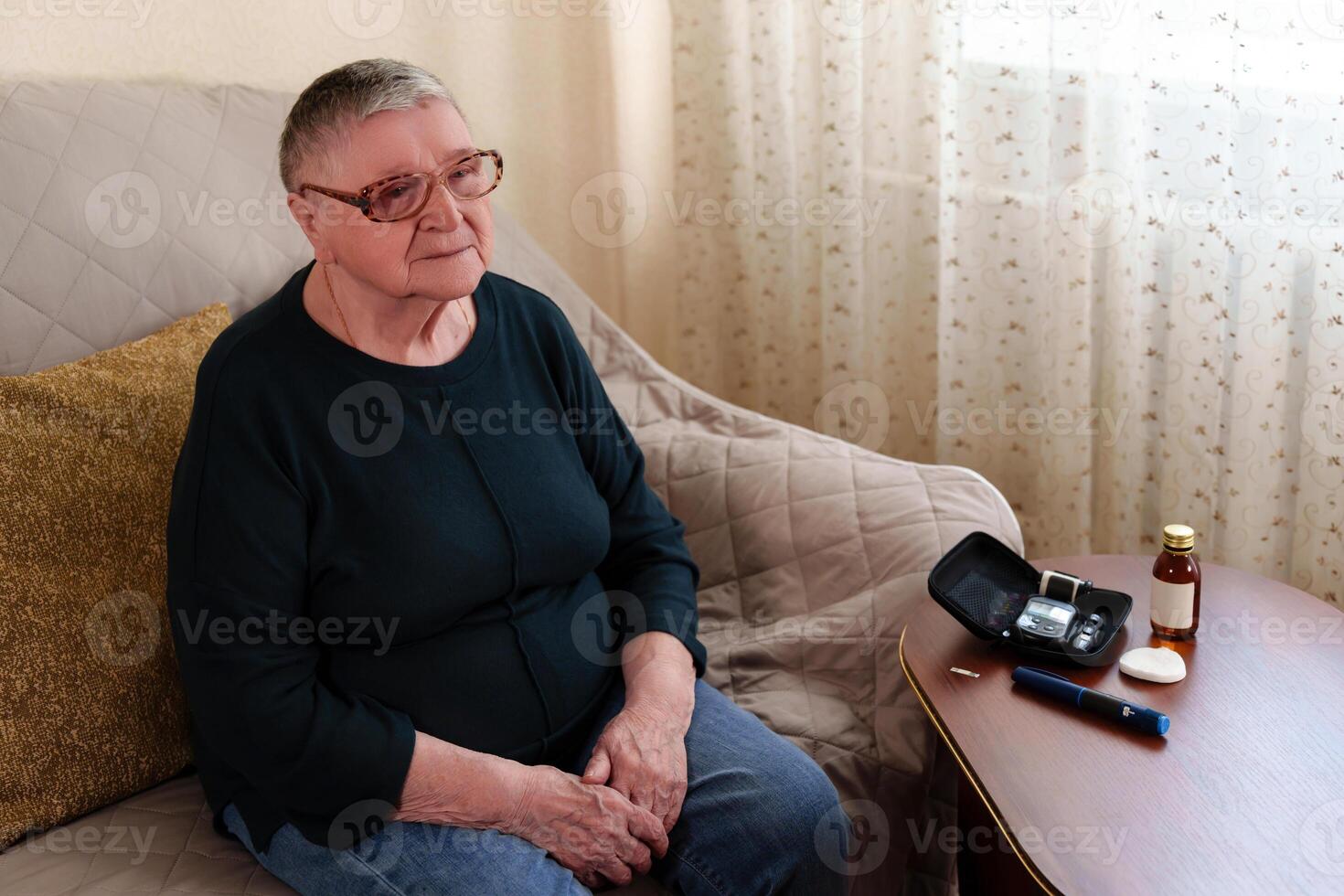 baby boomer with short gray hair and glasses sits on a sofa, a blood sugar measuring machine and an insulin syringe-pen are on the table next to her photo