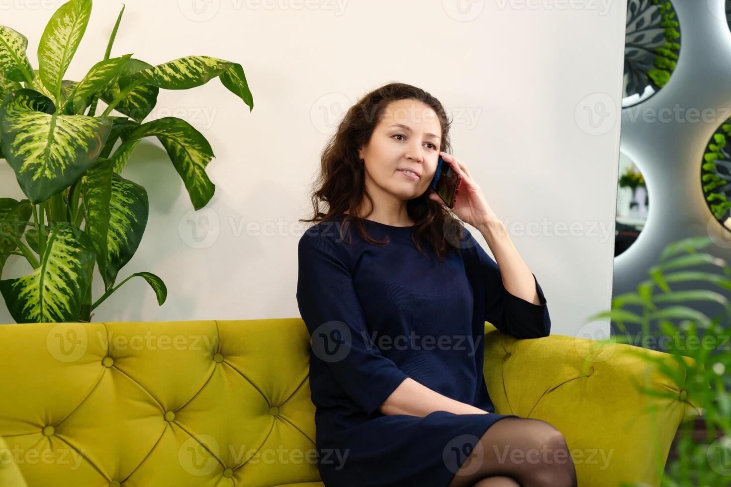 Serious and professional middle-aged woman talking on the phone while sitting on a sofa in a modern office, conveying the image of an experienced executive photo
