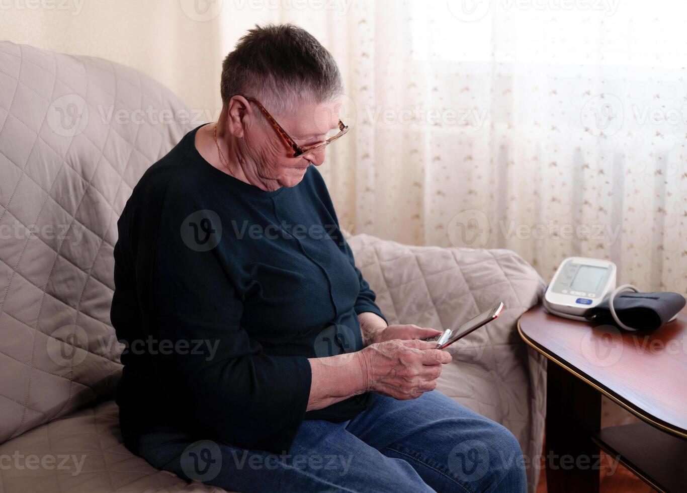 baby boomer generation sits on the couch talking about health with loved ones on the phone, with a blood pressure machine next to them photo