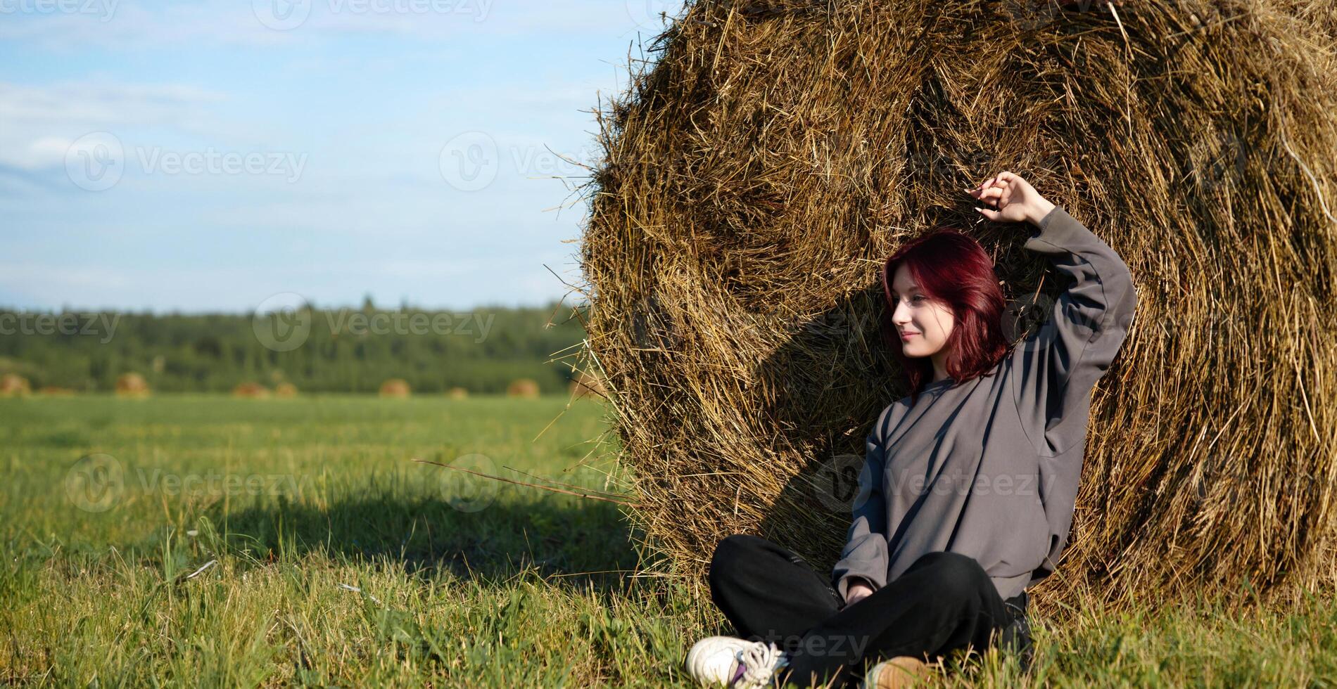 Teenager enjoying solitude in a field sitting leaning against a haystack, summer, afternoon photo