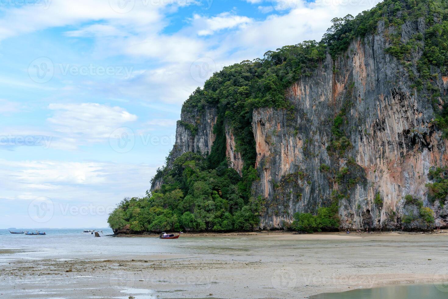 coastline revealed as the low tide recedes, In the distance, a small boat gently sways on the calm waters near rocky cliffs photo