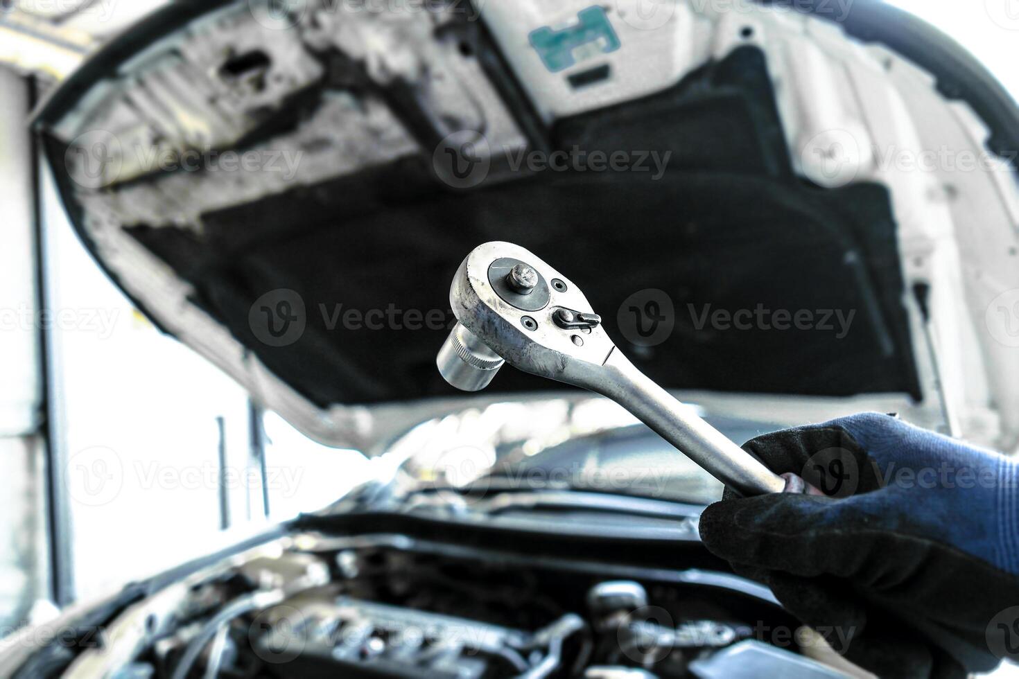 Mechanic is repairing a car engine , Auto mechanic hand holds a socket wrench with blurred car engine compartment in the background , car repair concept photo