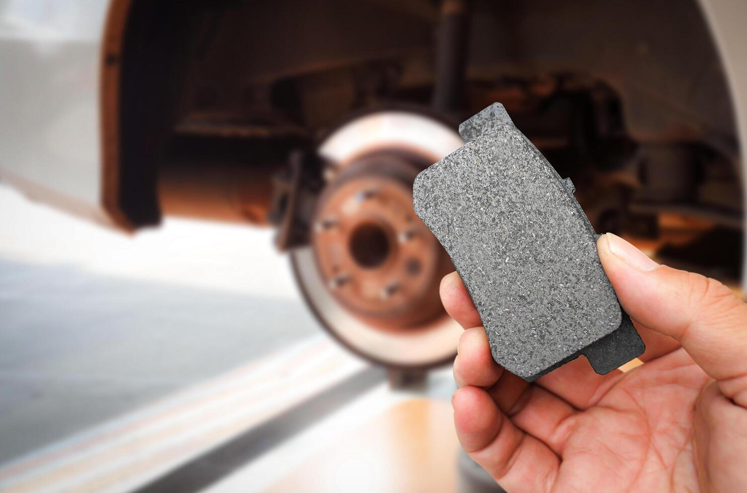 Car brake system maintenance concept , mechanic hand holding a car brake pad with braking system of an automobile without a wheel on background photo
