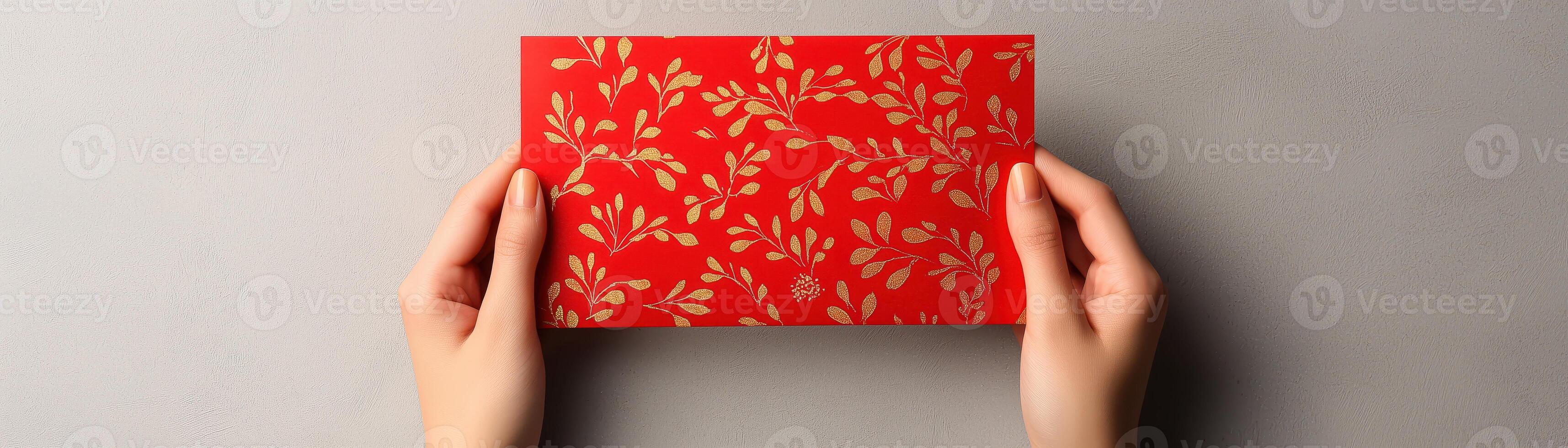 A pair of hands holding a vibrant red envelope with a floral pattern against a neutral background, perfect for invitations and special occasions. photo