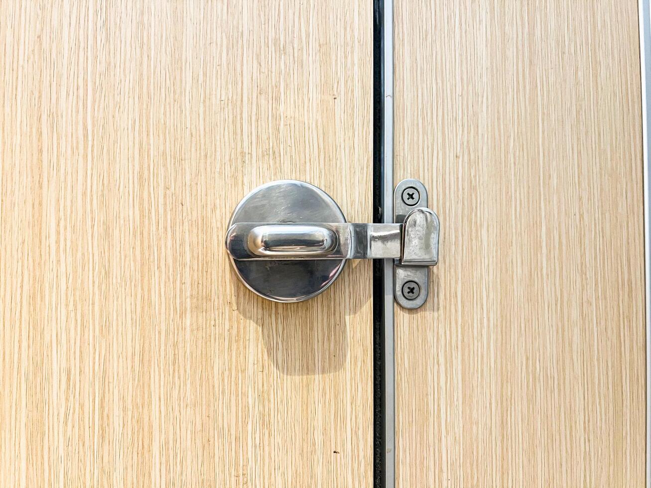 Minimalist stainless steel door latch on a wood-textured door, great for architecture, home improvement, and security topics photo