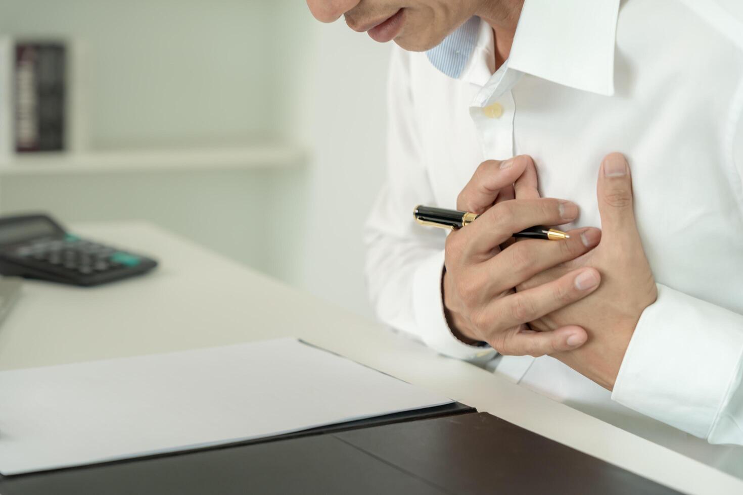 hand hold chest with heart attack symptoms, asian man working hard have chest pain caused by heart disease, leak, dilatation, enlarged coronary heart, press on the chest with a painful expression photo