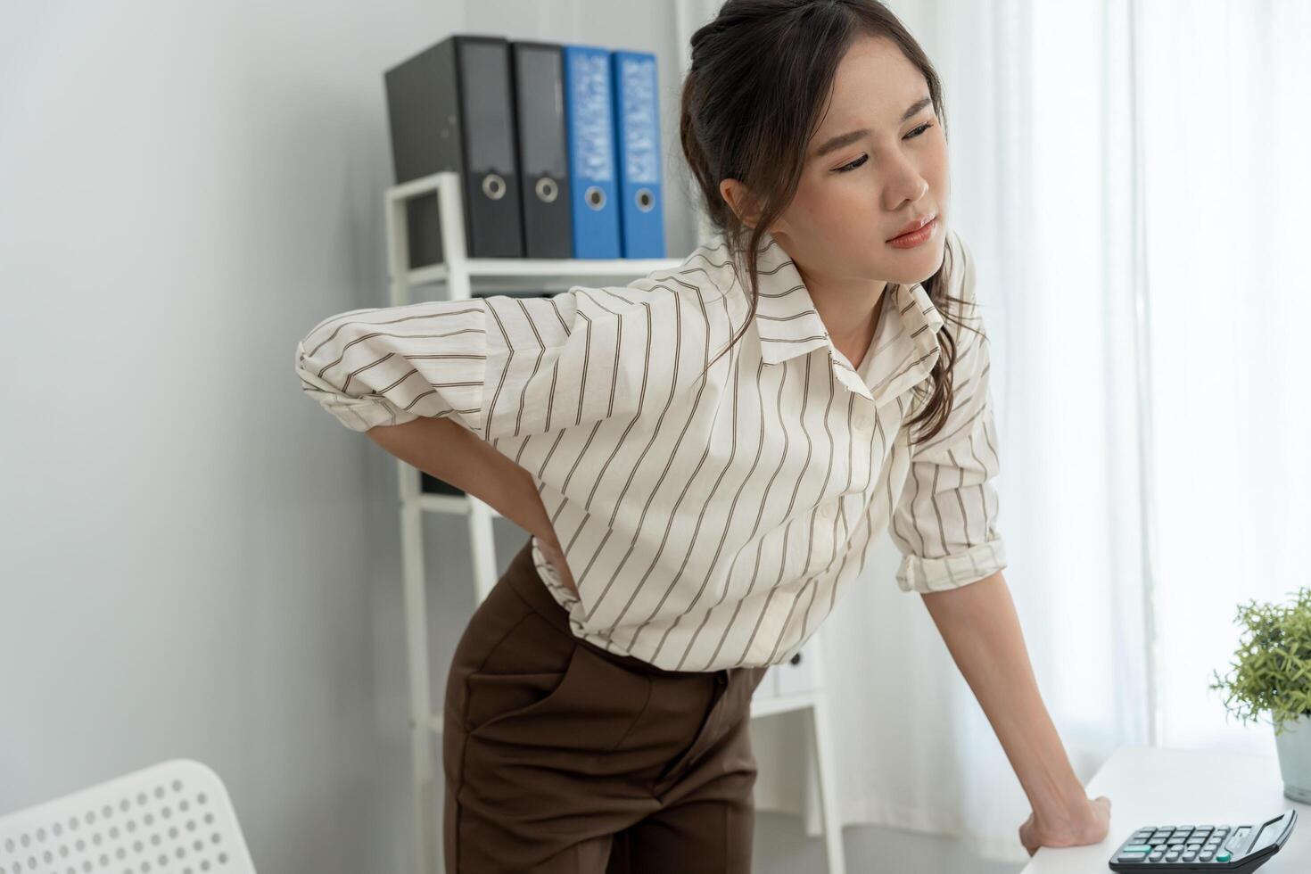 Asia beautiful woman holding her lower back while and suffer from unbearable pain health and problems, chronic back pain, backache in office syndrome, scoliosis, herniated disc, muscle inflammation photo