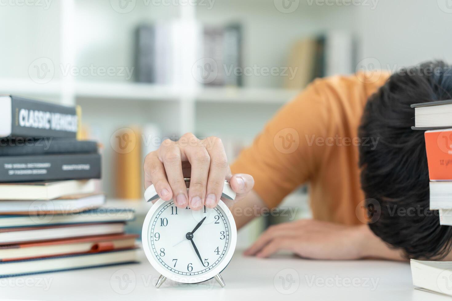 Asian student man turns off the alarm clock because he is tired from reading, male prepare for test and learning lessons in the library. stress, despair, haste, misunderstanding reading, discouraged. photo