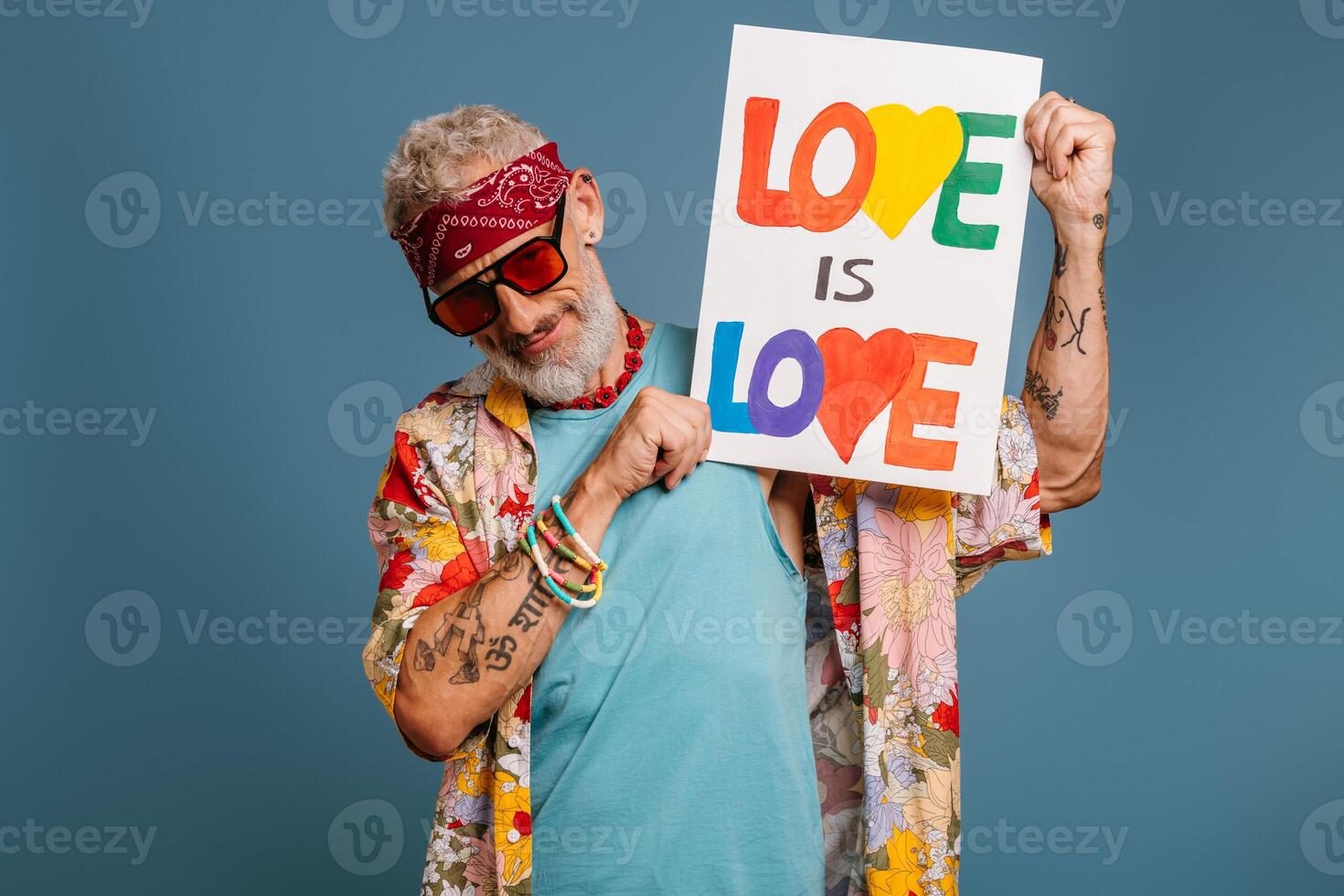 Cool hipster senior man in funky shirt showing colorful banner and smiling against blue background photo
